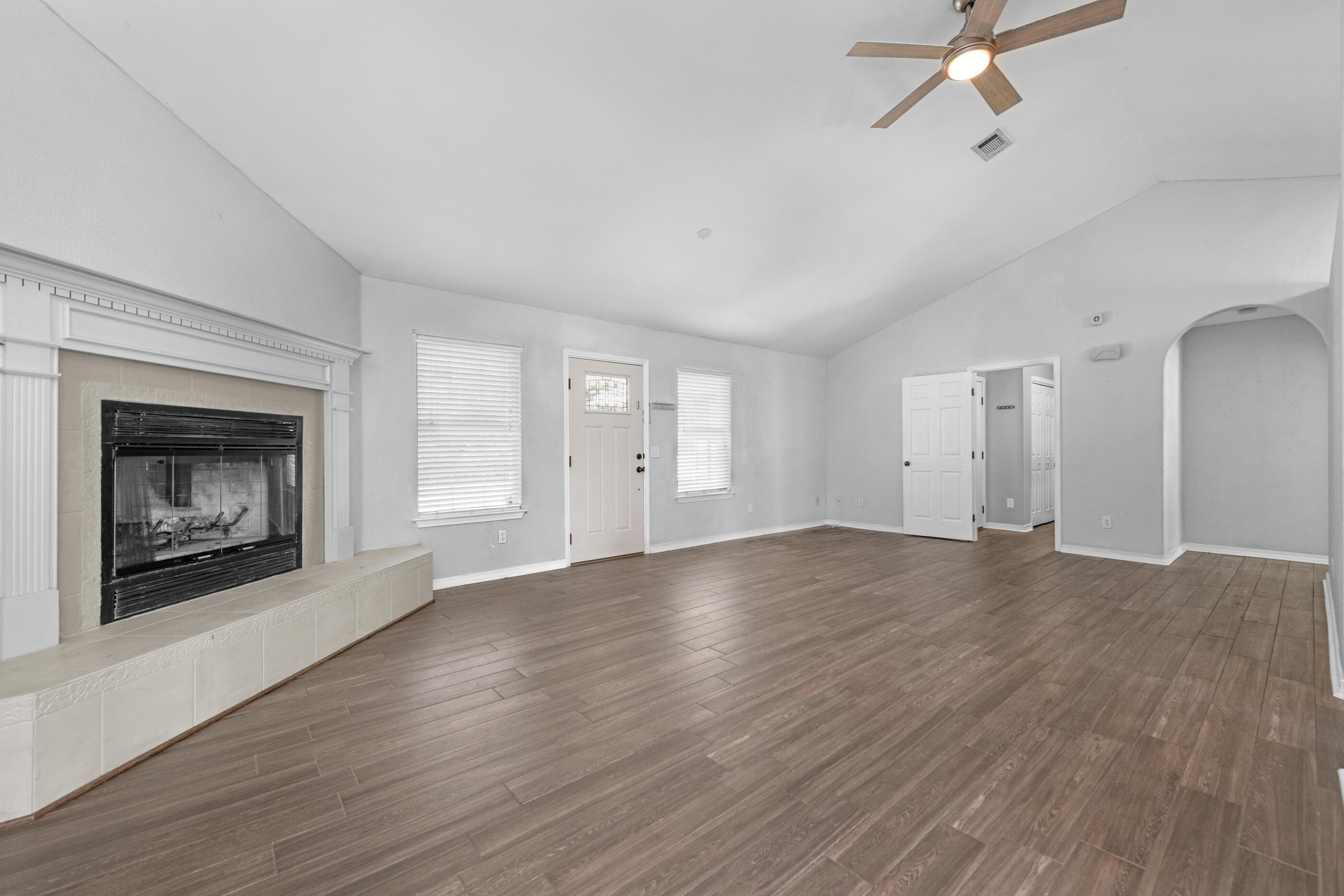 an empty room with wooden floor fireplace and windows