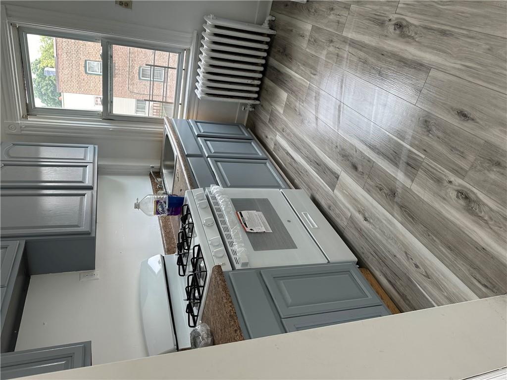 Kitchen featuring radiator, gray cabinetry, white gas stove, and light wood-type flooring