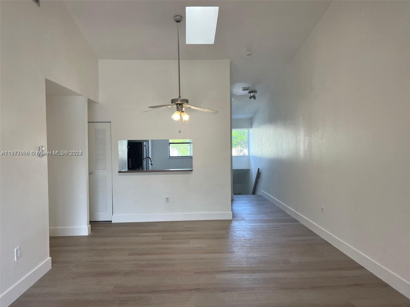 a view of an empty room with wooden floor and a ceiling fan