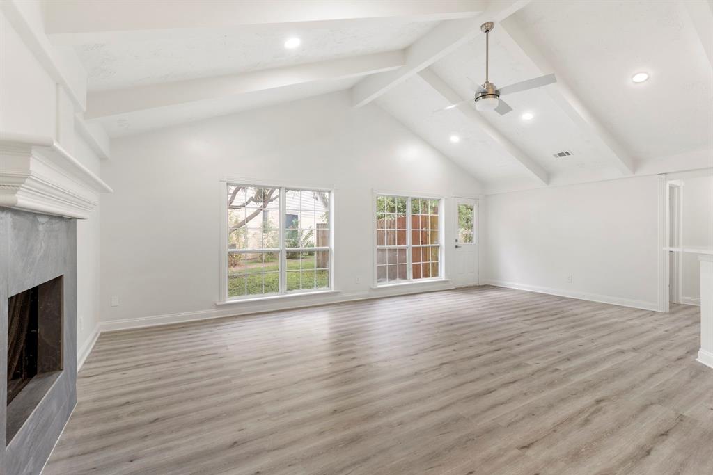 an empty room with wooden floor fireplace and windows