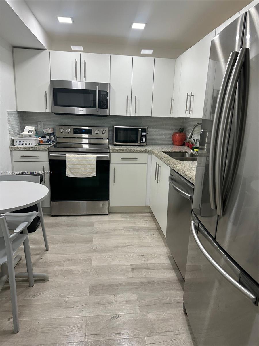 a kitchen with granite countertop a refrigerator stove and white cabinets