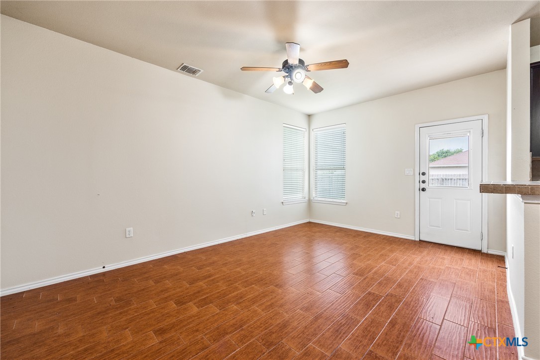 an empty room with wooden floor chandelier fan and windows