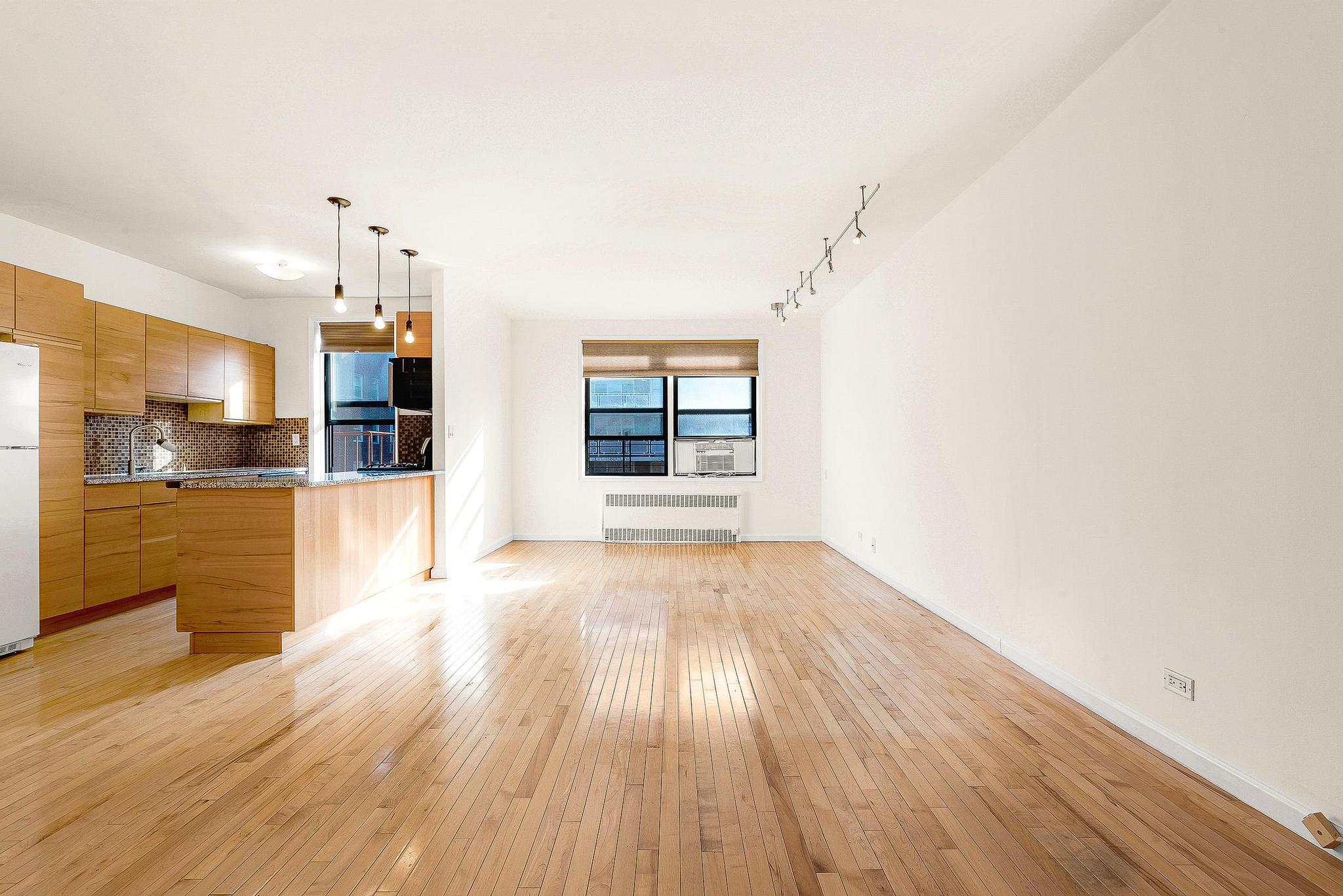 a view of a living room with wooden floor and kitchen view