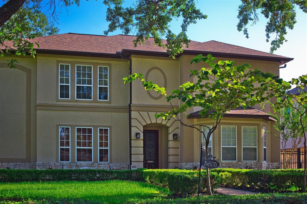 This is a two-story home features a mix of brick and Stucco with gated drive suggesting a private and secure environment. The house is complemented by a well-manicured lawn and mature trees, creating an inviting suburban atmosphere in the heart of Bellaire.