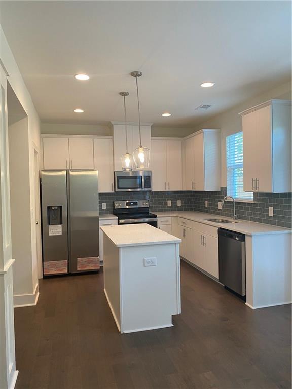 a kitchen with stainless steel appliances kitchen island granite countertop a refrigerator a sink dishwasher a stove with white cabinets