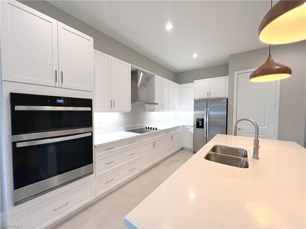 Kitchen featuring white cabinets, stainless steel appliances, sink, wall chimney exhaust hood, and pendant lighting