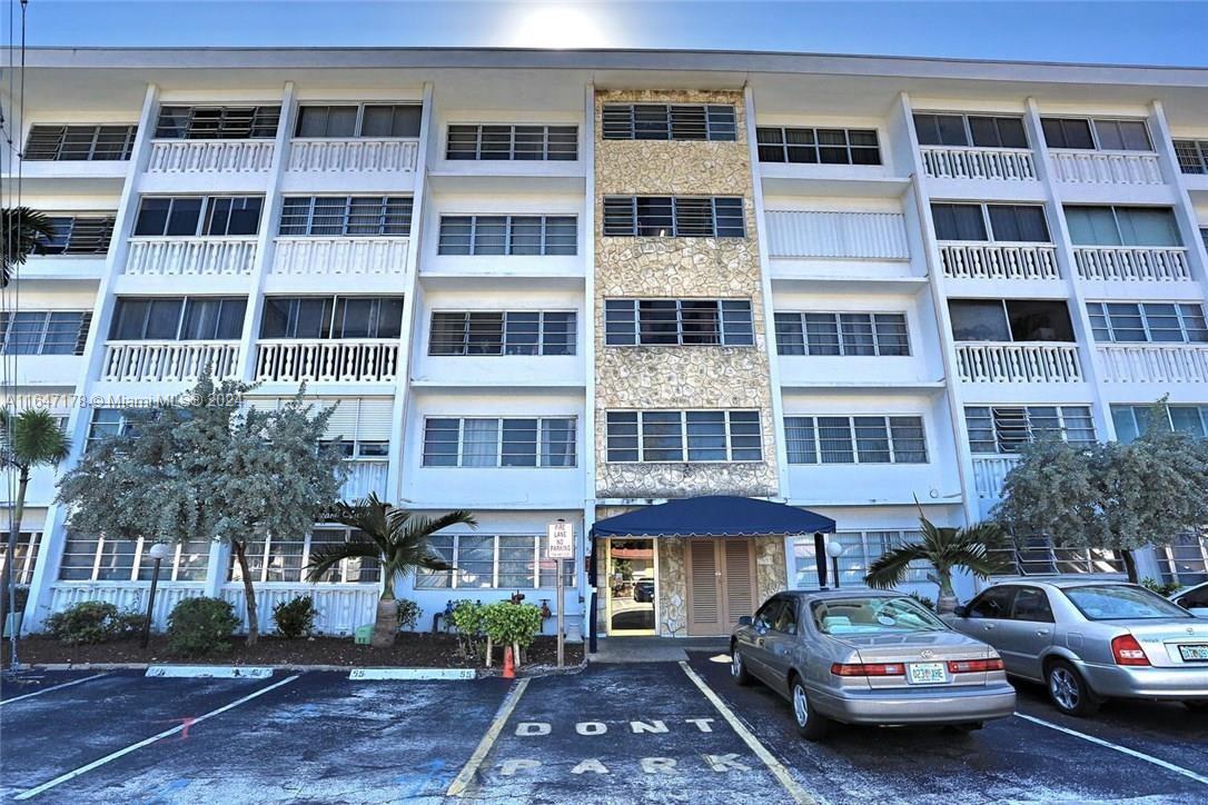 a front view of a building with lot of cars and trees