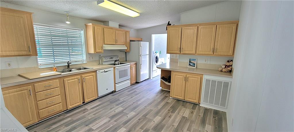 Kitchen with white appliances, sink, a textured ceiling, lofted ceiling, and hardwood / wood-style flooring