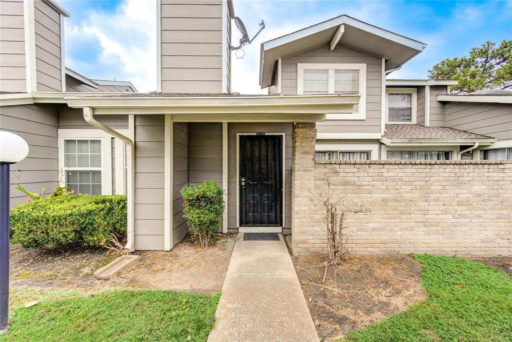 This is a front view of a two-story townhouse featuring a neutral color palette with a combination of siding and brickwork. It includes a covered entryway, a security door, and modest landscaping.