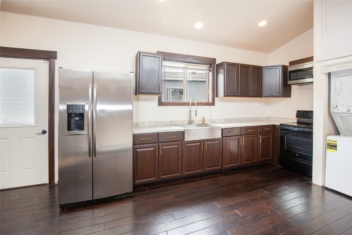 Kitchen featuring dark brown cabinets, stacked washing maching and dryer, sink, lofted ceiling, and appliances with stainless steel finishes