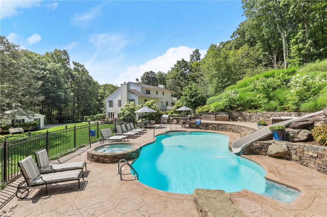 View of pool featuring a patio, a water slide, lawn, and an in ground hot tub