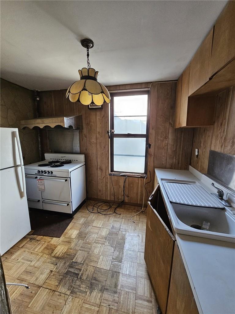 Kitchen featuring pendant lighting, wooden walls, white appliances, sink, and light parquet floors