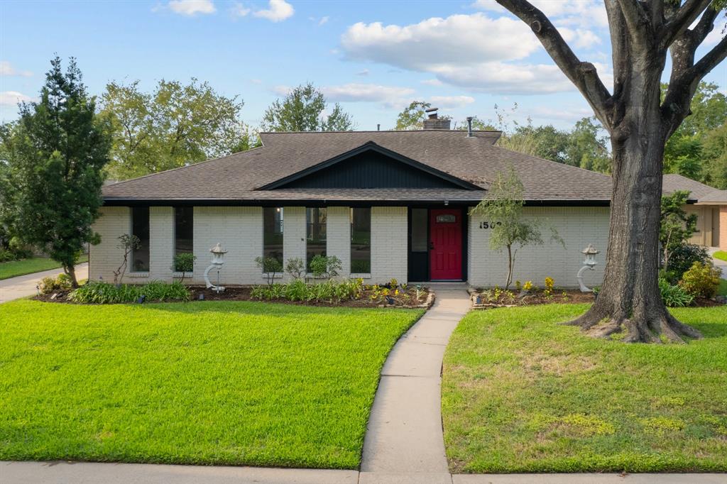 Charming single-story brick home with a welcoming new red front door, neat landscaping, and mature trees in a serene neighborhood.