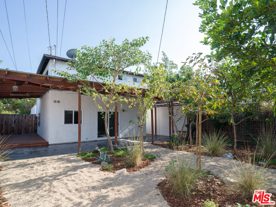 a view of a house with brick walls plants and large tree