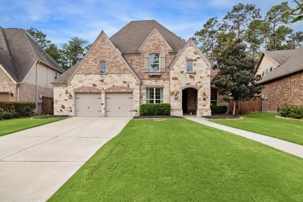 This is a spacious two-story brick & stone home featuring a double garage, arched entryway, and a well-manicured lawn, nestled in a residential neighborhood with tall trees.