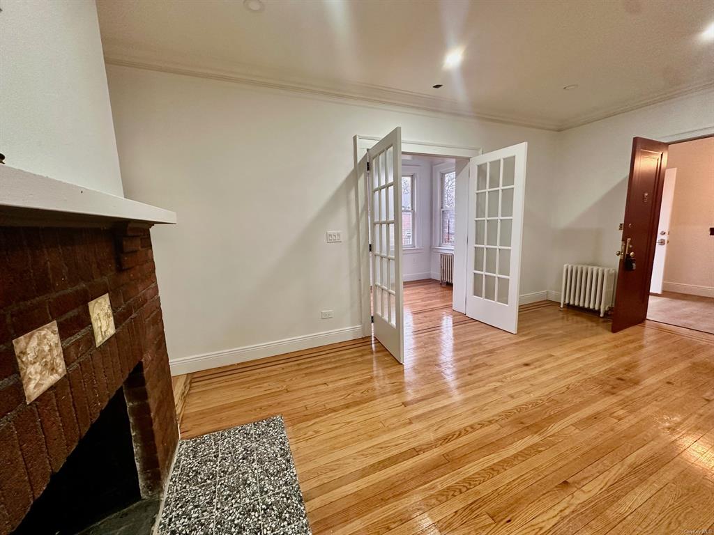 Living room featuring radiator, french doors, a brick fireplace, light wood-type flooring, and ornamental molding