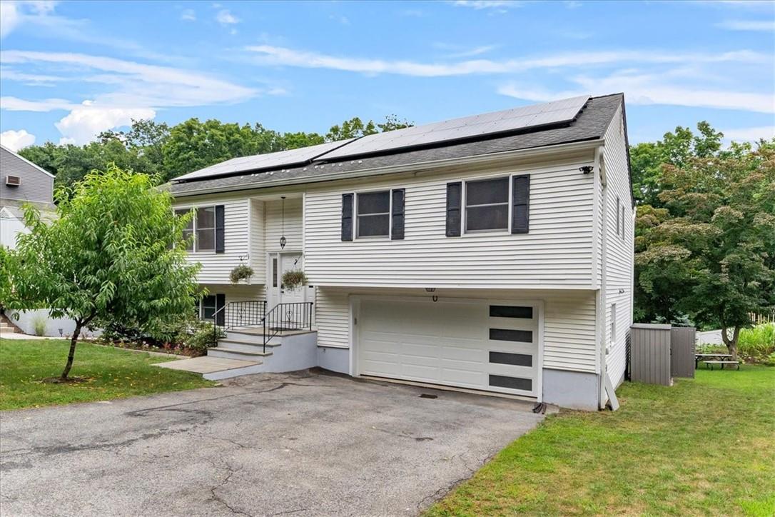 Bi-level home featuring a garage, a front lawn, and solar panels