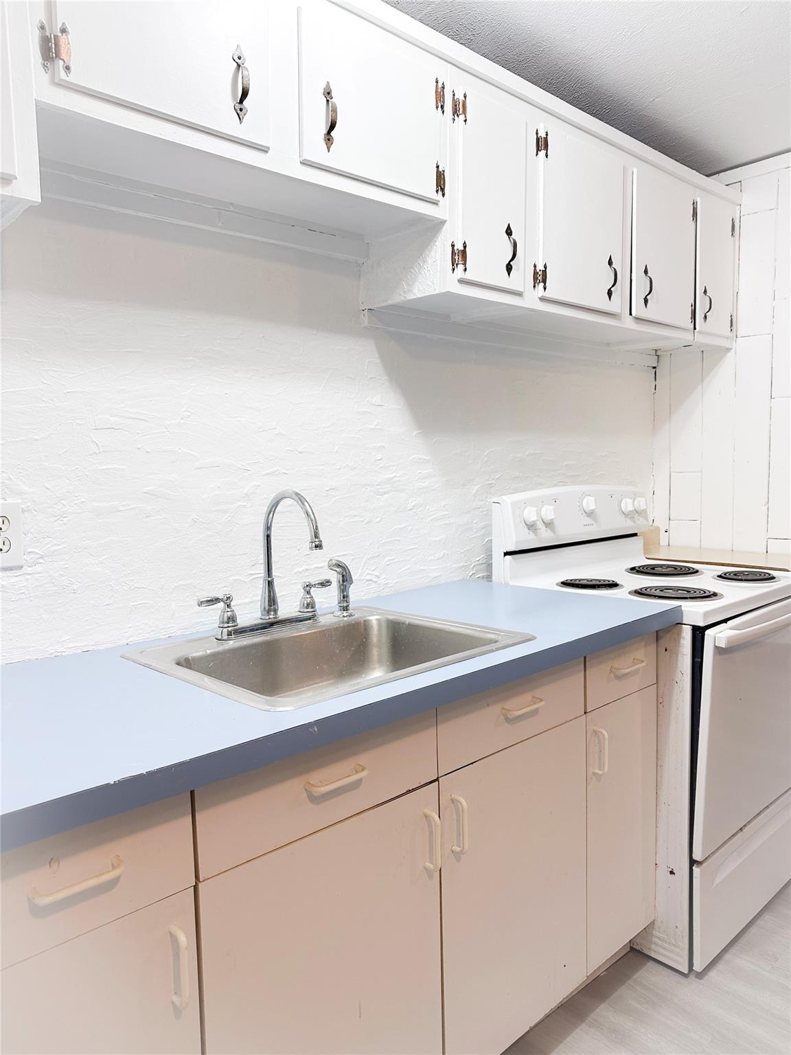 Kitchen featuring white range with electric cooktop, light hardwood / wood-style flooring, white cabinets, and sink