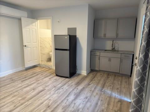 Kitchen featuring gray cabinets, light wood-type flooring, sink, and stainless steel refrigerator