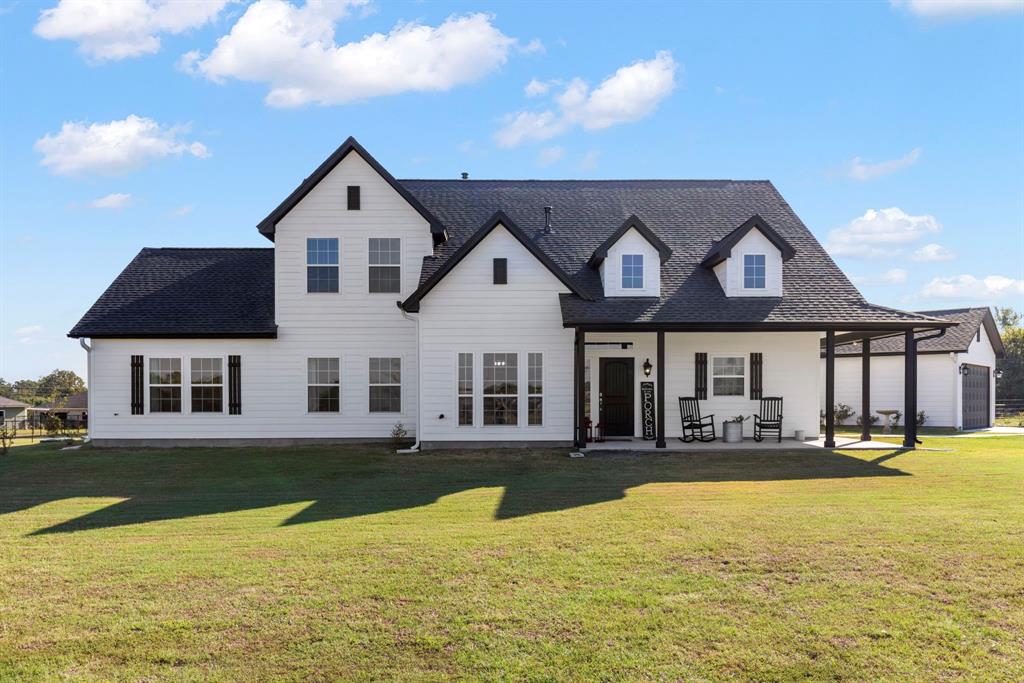 This spacious two-story home has a white exterior and black accents, featuring a large covered porch and a sizeable yard!