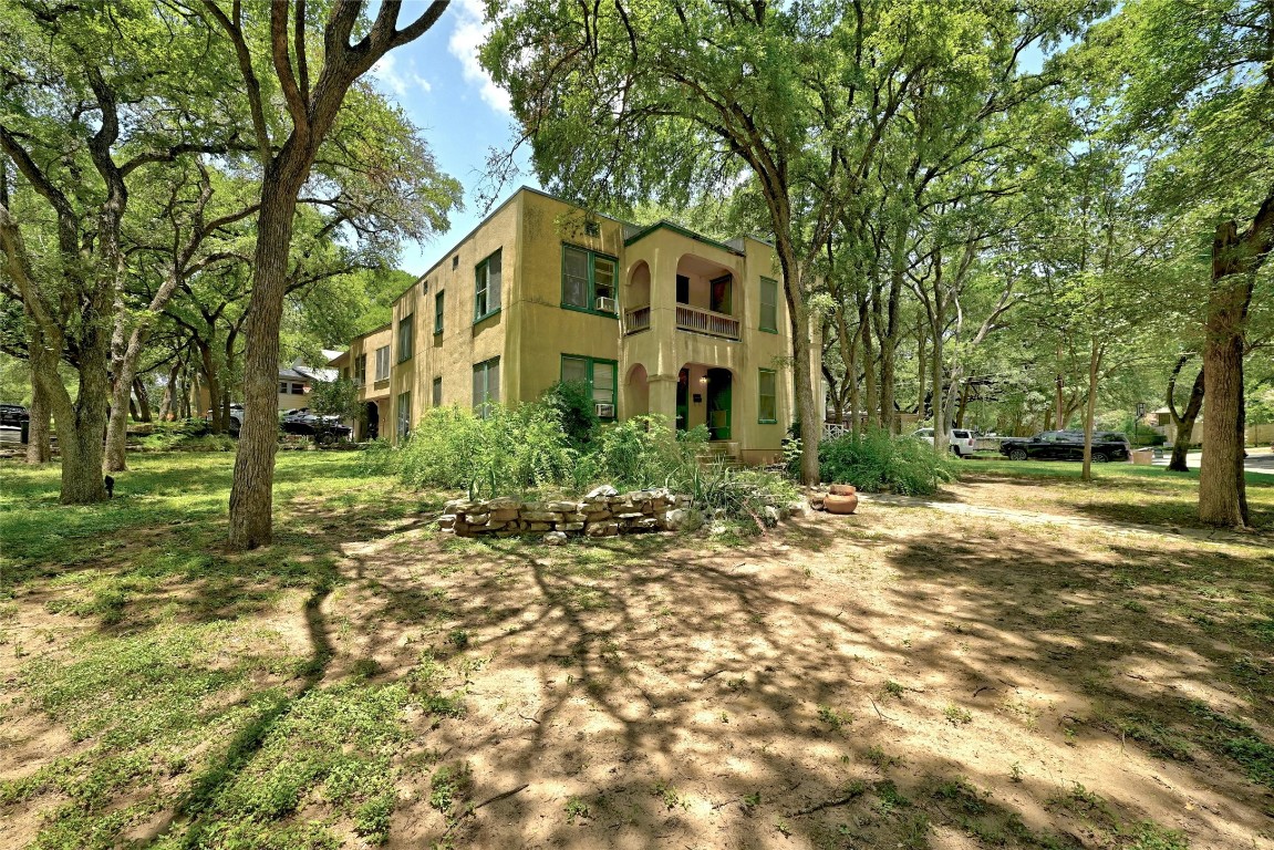 a view of a white house next to a yard with big trees