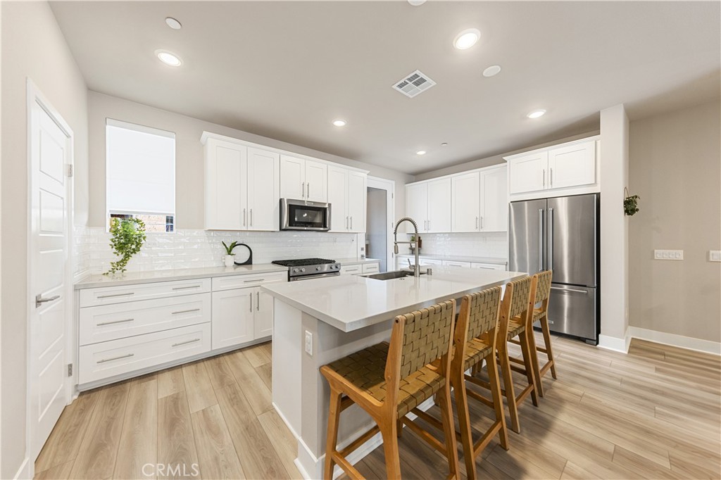 a kitchen with stainless steel appliances kitchen island granite countertop a white stove top oven and white cabinets with wooden floor