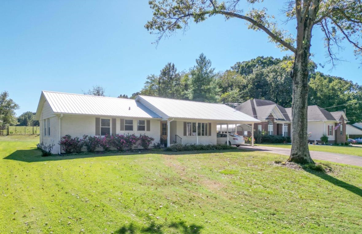 a view of a house next to a big yard and large trees