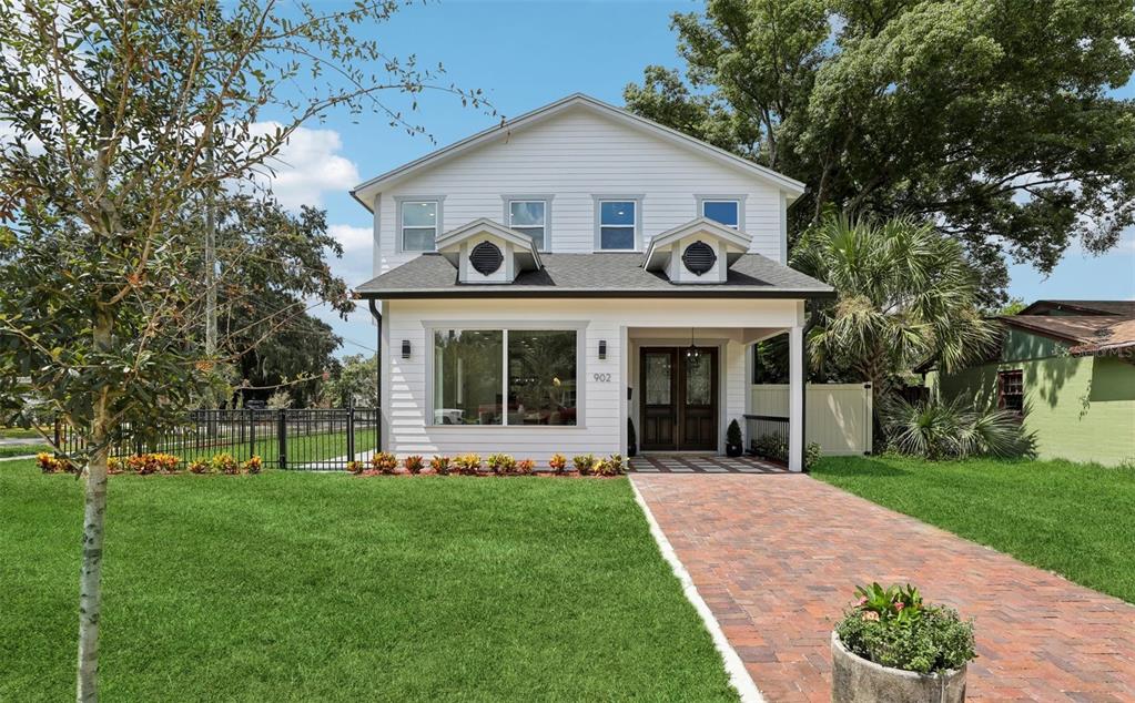 a view of a white house with a big yard potted plants and large tree