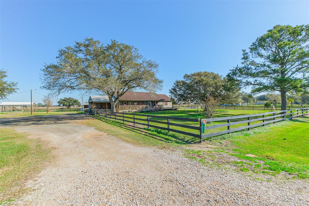 Driveway view of property as seen driving south on Foster Road. A three-rail wood fence surrounds the house and a couple of small outbuildings in a decorative fashion. Smooth wire, and barbed-wire fencing and cross-fencing provides the perimeter fencing.