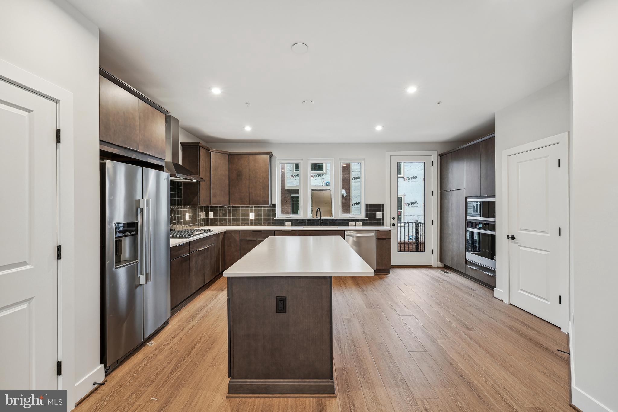 a large kitchen with a center island wooden floor stainless steel appliances and cabinets