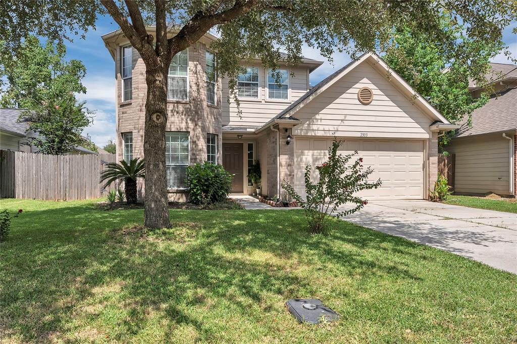 This is a two-story home featuring a mix of stone and siding, a two-car garage, and a well-maintained lawn with mature trees.