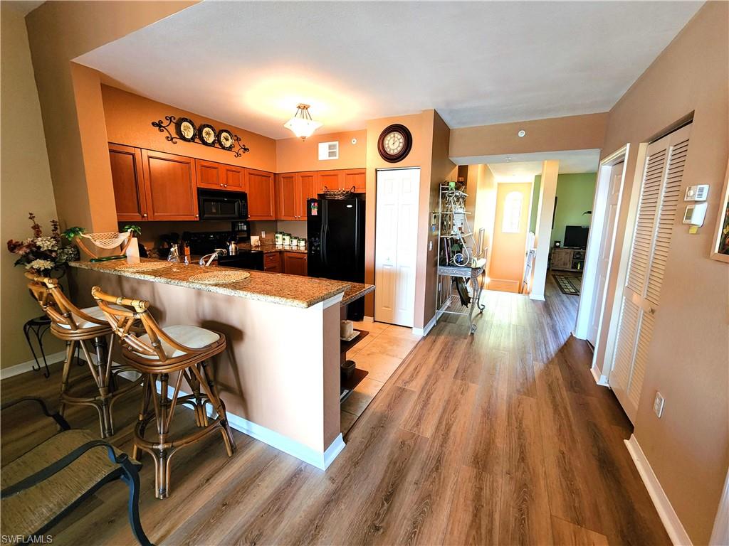 Kitchen with kitchen peninsula, black appliances, a kitchen bar, light wood-type flooring, and light stone counters