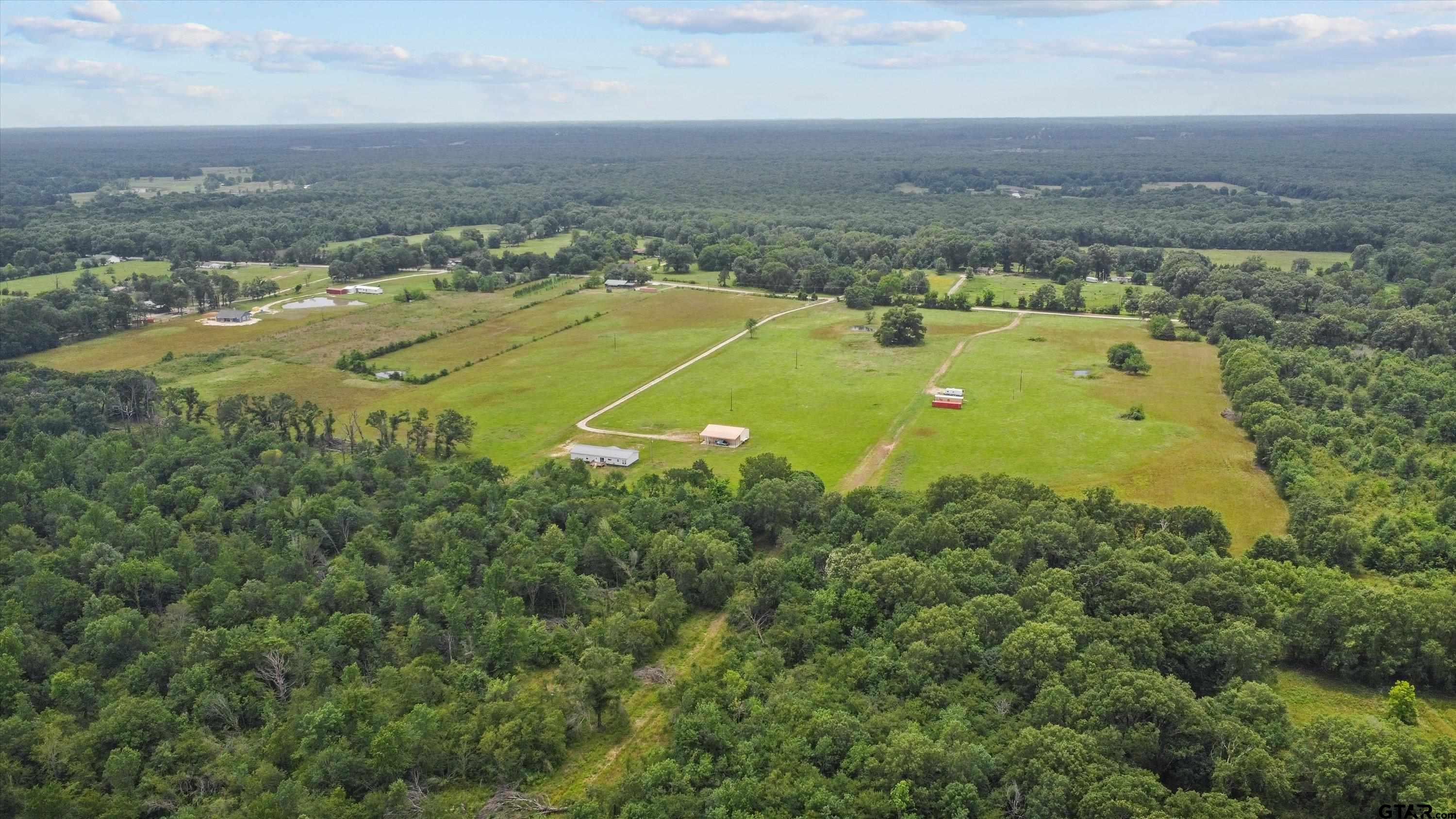 an aerial view of a residential houses with outdoor space and trees all around