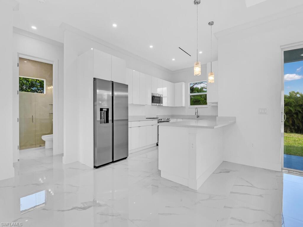 Kitchen with white cabinetry, appliances with stainless steel finishes, hanging light fixtures, sink, and kitchen peninsula