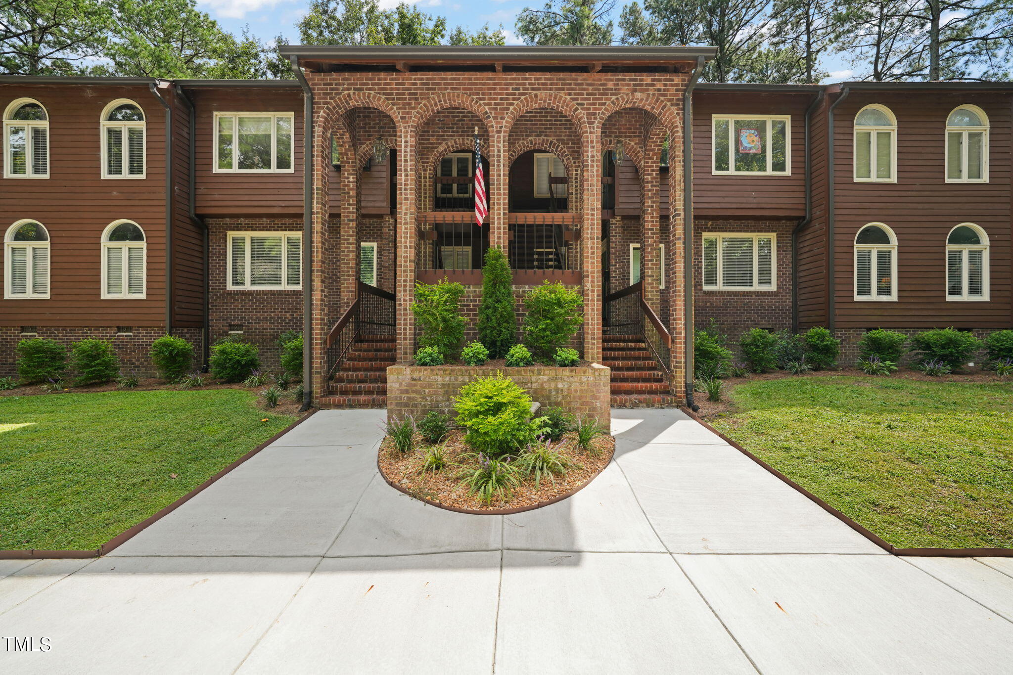 a view of a brick house with a yard plants and large tree