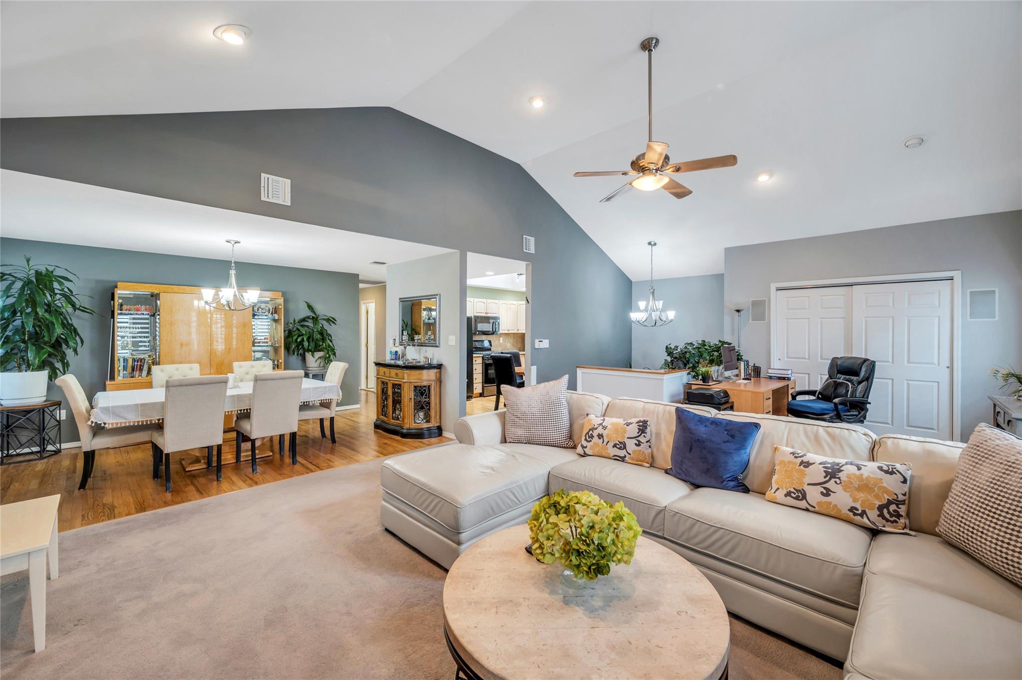 Living room featuring ceiling fan with notable chandelier, wood-type flooring, and high vaulted ceiling