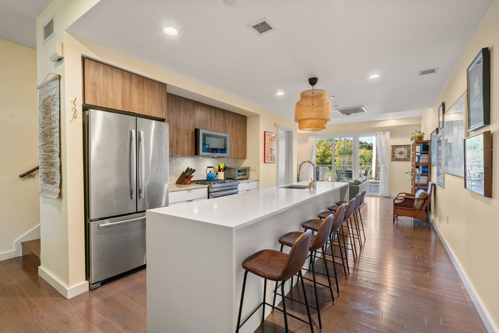 a kitchen with stainless steel appliances a refrigerator a sink dishwasher a dining table and chairs with wooden floor