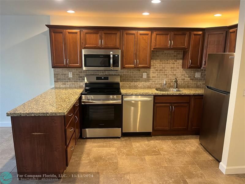 a kitchen with stainless steel appliances granite countertop a stove a sink dishwasher a refrigerator and a microwave