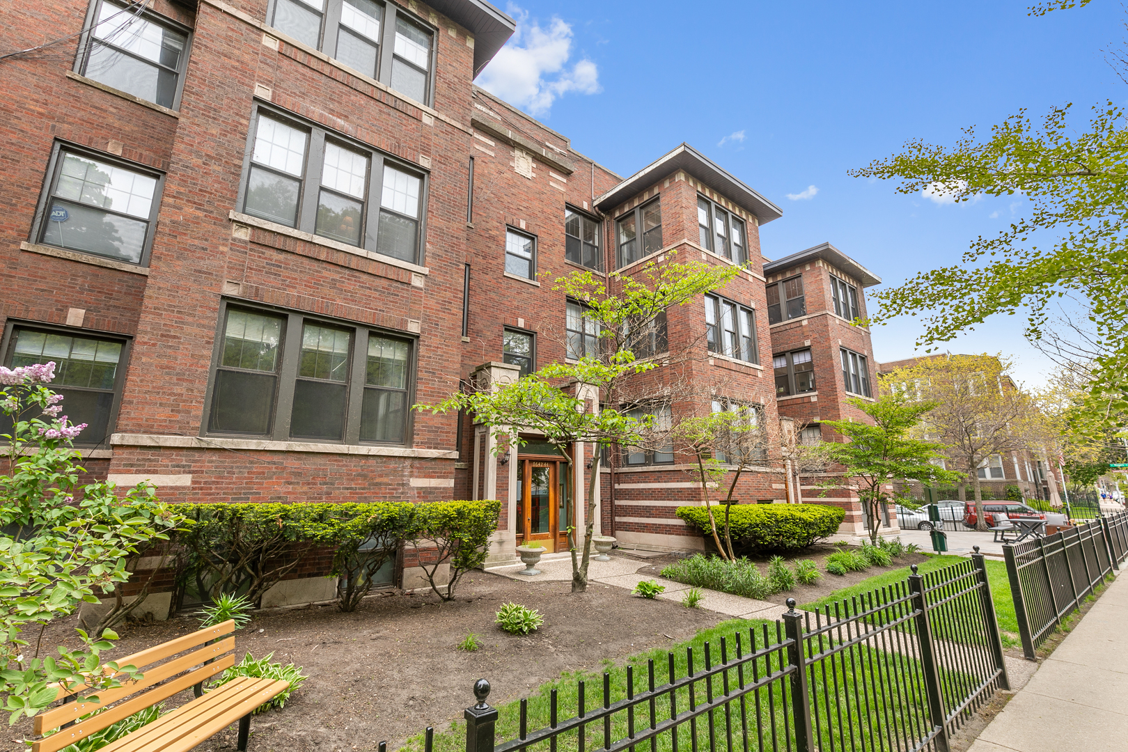 a view of a brick house with many windows plants and a bench