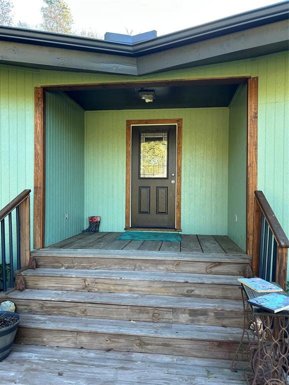 This inviting entryway features a charming wooden porch with stairs leading up to a front door framed by green siding and natural wood accents. A welcoming touch for any home buyer.