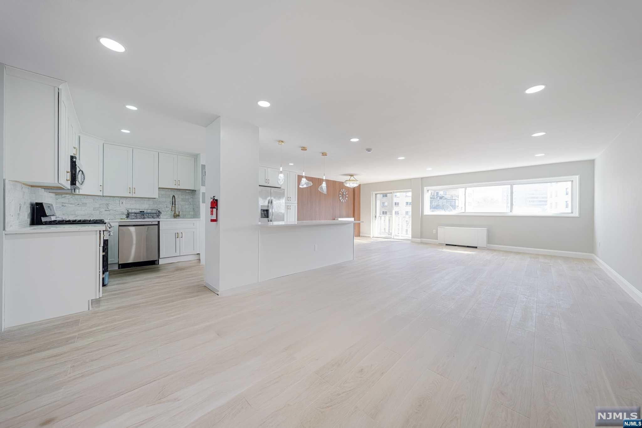 a view of an empty room with kitchen and window