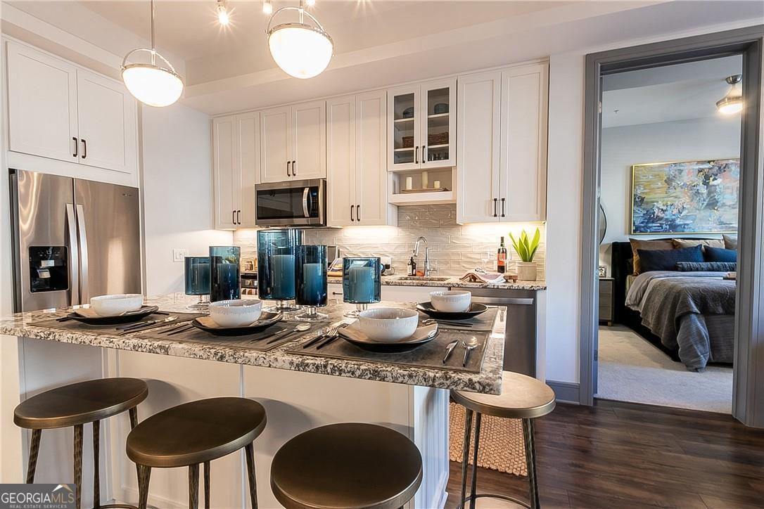 Kitchen featuring pendant lighting, dark hardwood / wood-style floors, a breakfast bar, white cabinetry, and stainless steel appliances