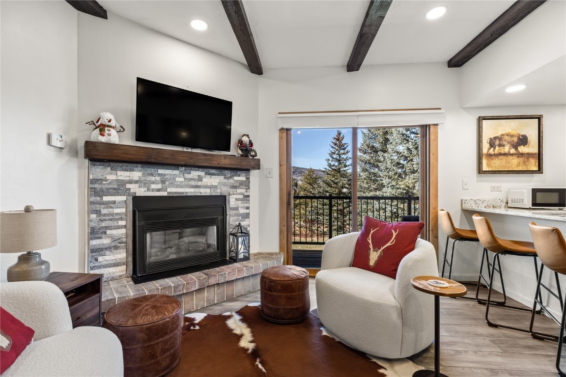 Living room featuring light wood-type flooring, a fireplace, and beam ceiling