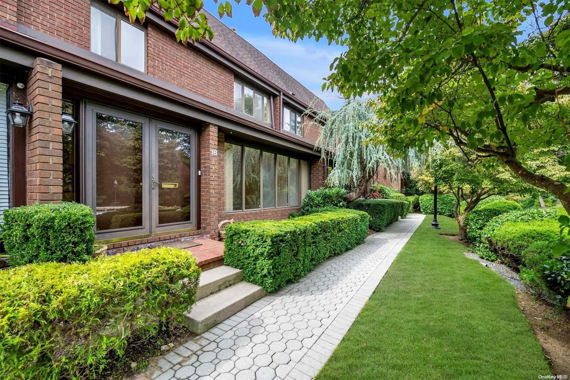 a view of a house with brick walls plants and large tree