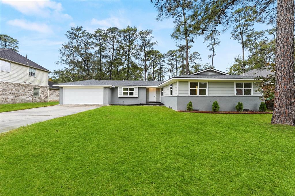 A view of the home’s facade with a spacious driveway, garage, and well-kept landscaping.