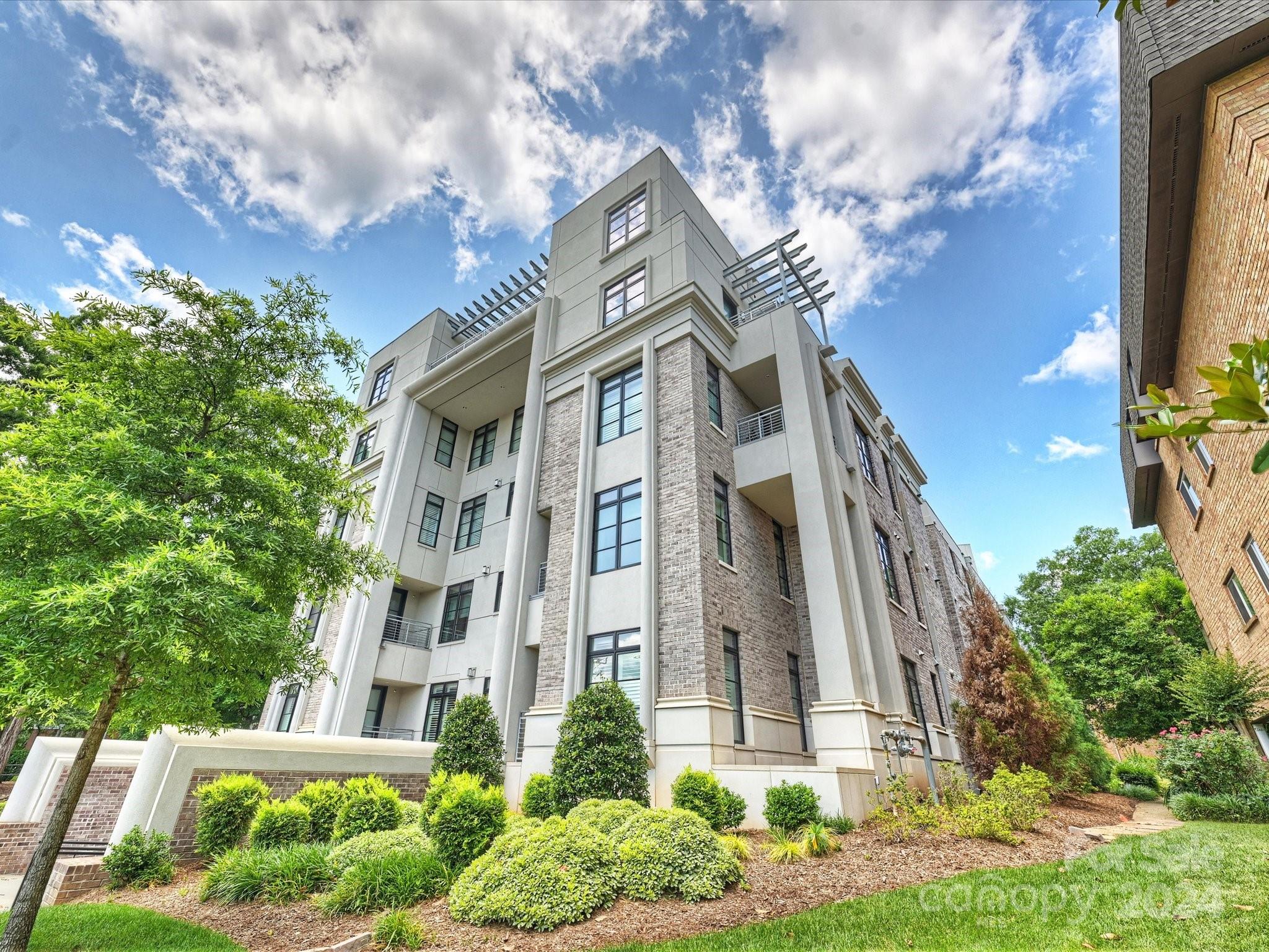 a front view of a multi story residential apartment building with yard and parking