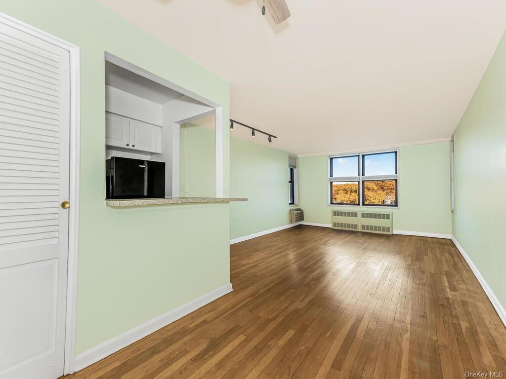 Unfurnished living room featuring a wall unit AC, radiator, rail lighting, and dark hardwood / wood-style flooring