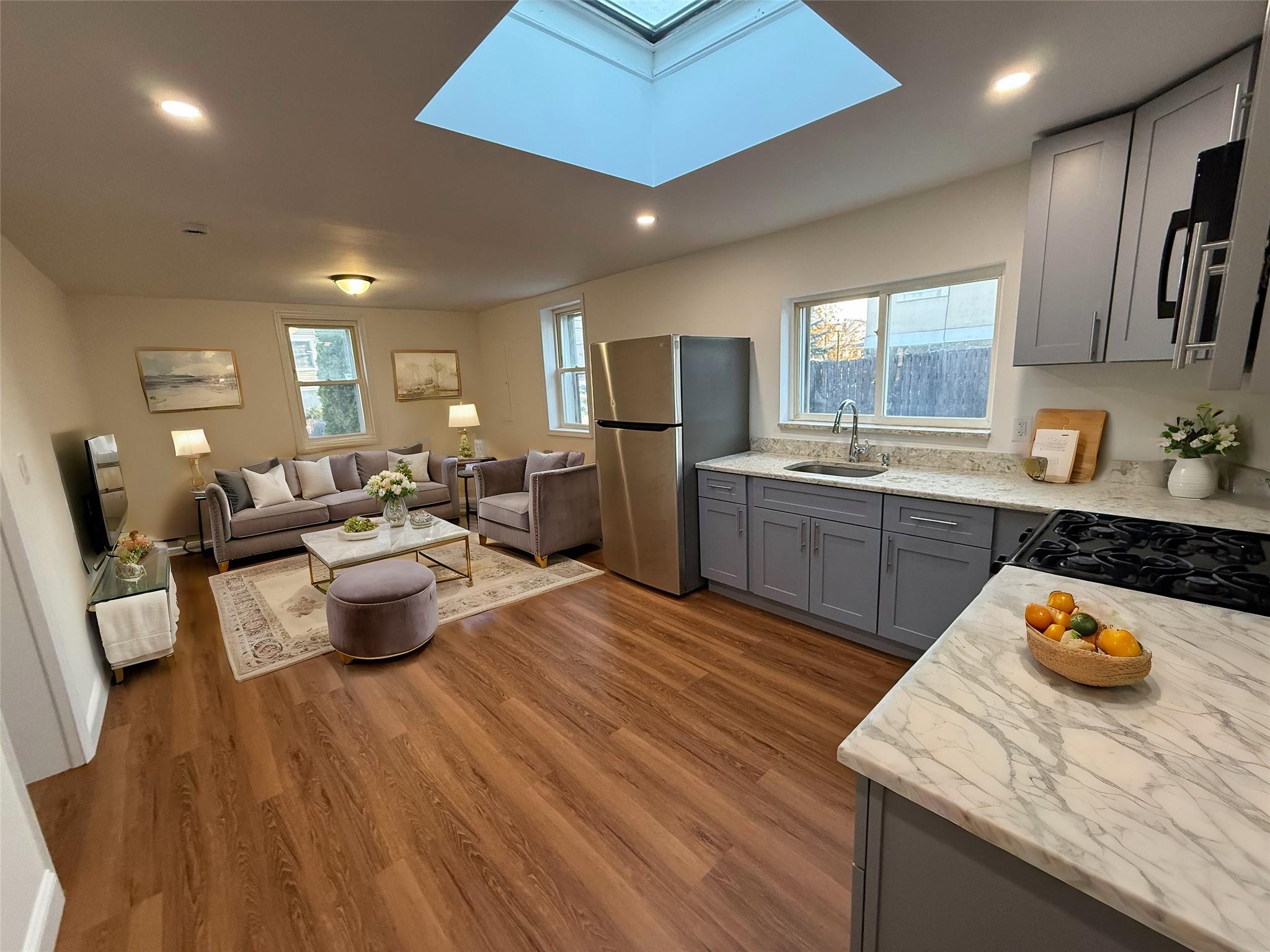 Virtually Staged - Living Room with open-concept Kitchen featuring hardwood / wood-style floors, plenty of natural light, sink, and a skylight