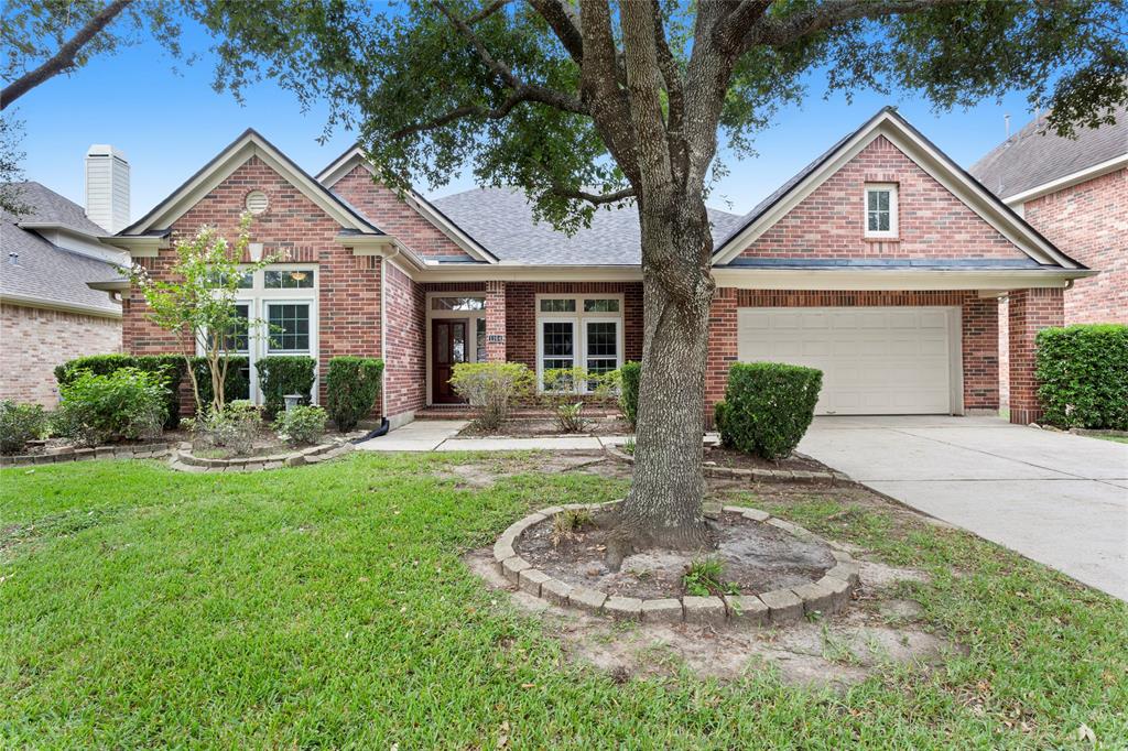 This is a single-story brick home with a 3 car tandem garage, featuring a well-maintained front yard with mature trees and landscaping.