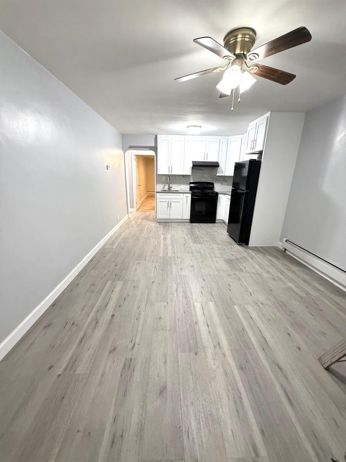 Kitchen featuring light wood-type flooring, ceiling fan, sink, black appliances, and white cabinetry